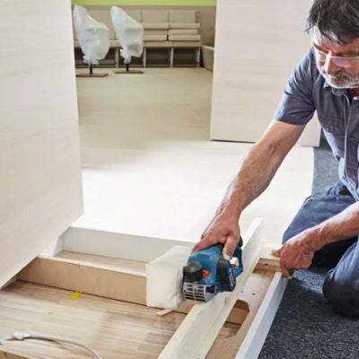 Homem usando ferramenta elétrica azul para trabalhar madeira clara em ambiente interno