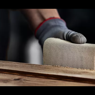 Pessoa a lixar madeira com luvas cinza e vermelhas e lixa creme.
