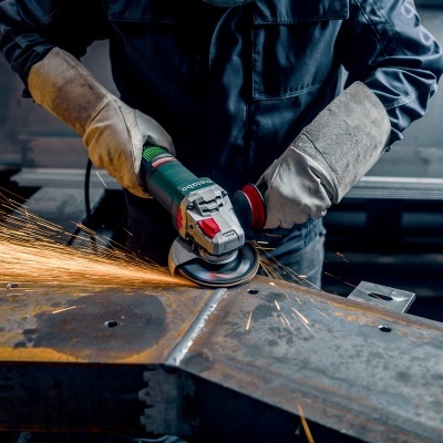 Pessoa usando luvas a operar esmerilhadeira em peça metálica com faíscas