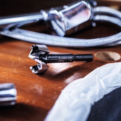 Broca preta sobre superfície de madeira com mangueira metálica e pia branca ao lado