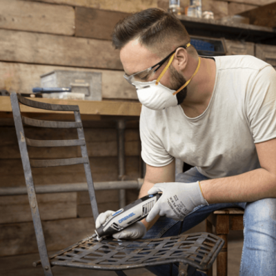 Homem a trabalhar metal com ferramenta elétrica numa oficina com parede de madeira