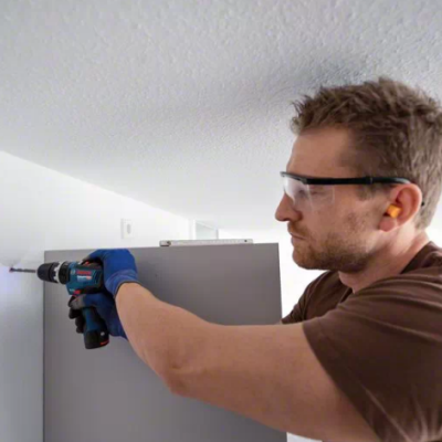 Homem a montar móvel de madeira cinzento com parafusadeira