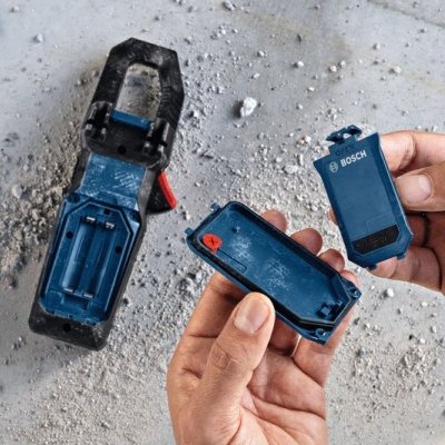 Dispositivo Bosch desmontado sobre superfície de cimento com mãos a segurá-lo