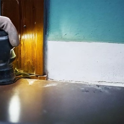 Mão com luva a usar lixadora elétrica numa superfície de madeira