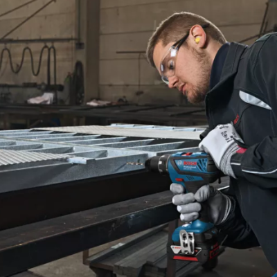 Homem a usar parafusadeira Bosch numa estrutura metálica cinza em ambiente industrial
