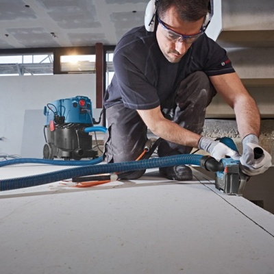 Homem a cortar placa de gesso com ferramenta elétrica em ambiente de construção