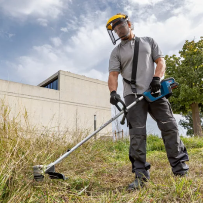 Homem a usar aparador de relva elétrico num terreno com relva alta
