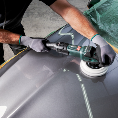 Pessoa a polir carro prateado com lixadora elétrica verde.