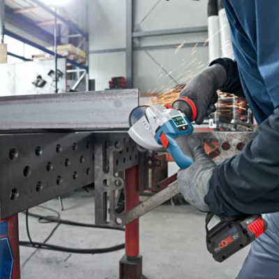 Trabalhador com rebarbadora a cortar peça metálica numa oficina industrial