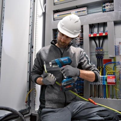 Homem com capacete branco a usar ferramenta elétrica Bosch em quadro elétrico
