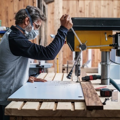 Homem a usar máquina de perfuração numa oficina de madeira