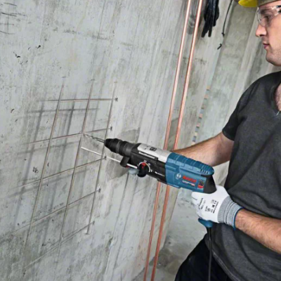 Homem a usar martelo perfurador eléctrico Bosch para furar parede cinzenta com grelha metálica