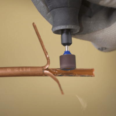 Mãos com luvas usando ferramenta rotativa para polir tubo de cobre