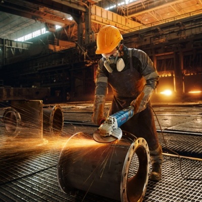 Trabalhador com equipamento de proteção operando esmerilhadora em tubo metálico numa fábrica