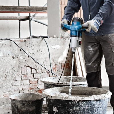 Homem a misturar material de construção em balde preto num local de obra