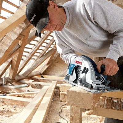 Homem a usar serra circular Bosch para cortar madeira em construção de telhado