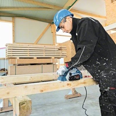 Homem com capacete azul a lixar madeira num ambiente de construção
