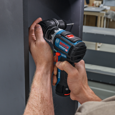 Parafusadeira Bosch Professional preta com detalhes azuis e vermelhos em mão a fixar peça de mobiliário