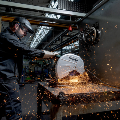 Homem a usar rebarbadora elétrica a cortar metal com faíscas em ambiente industrial