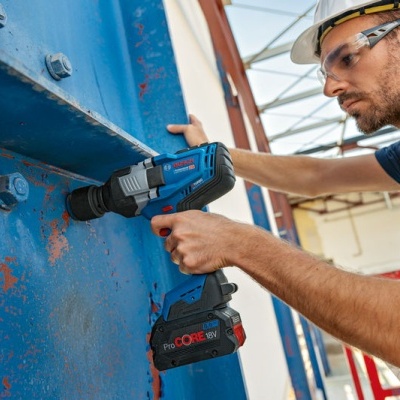 Homem com capacete e óculos de proteção a usar parafusadeira Bosch numa estrutura metálica azul