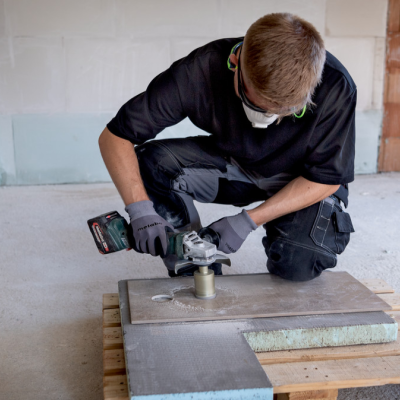 Trabalhador com luvas e máscara a usar ferramenta elétrica numa placa sobre pallet de madeira