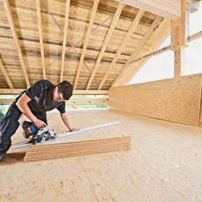 Homem a cortar madeira com serra circular num espaço com teto de madeira