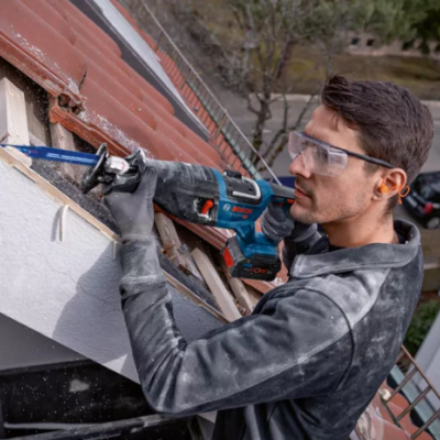 Homem a usar ferramenta elétrica na madeira da fachada de uma casa ao ar livre