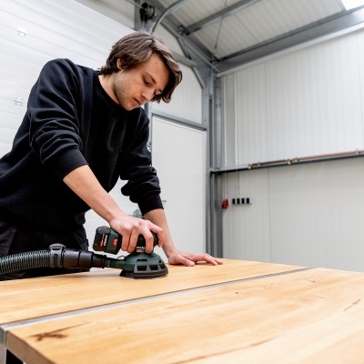 Homem a lixar mesa de madeira com lixadeira elétrica