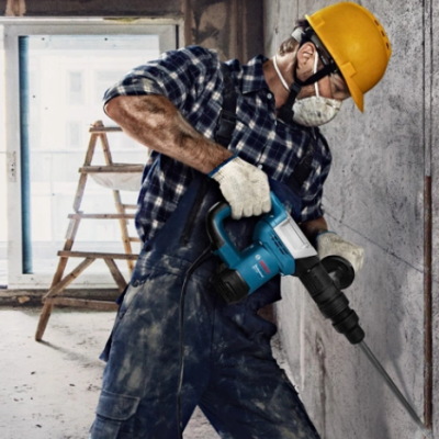 Trabalhador com capacete amarelo e martelo demolidor em obra interna