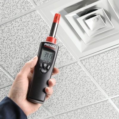 Detector portátil RIDGID com visor digital segurado à mão junto a teto de placas quadradas brancas