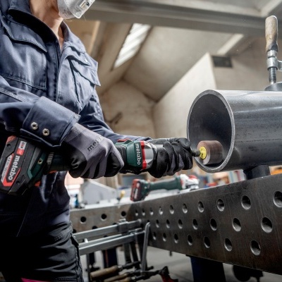 Pessoa a trabalhar com ferramenta elétrica Bosch num tubo metálico escuro em oficina.
