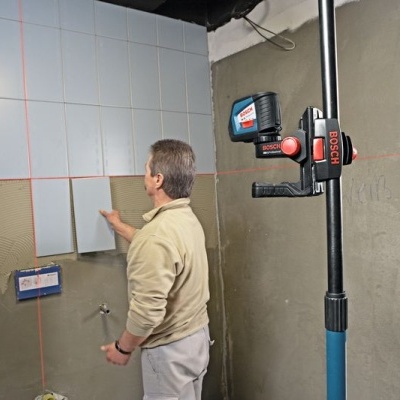 Homem a instalar azulejos brancos numa parede em construção com ferramenta Bosch ao lado