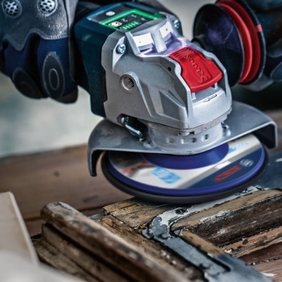 Esmerilhadora elétrica cinza com partes vermelhas e verdes a trabalhar em madeira