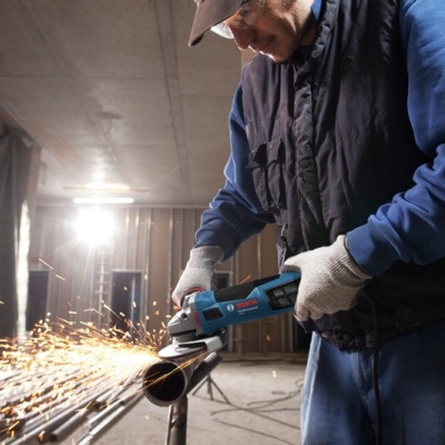 Homem a cortar tubo metálico com ferramenta elétrica azul e luvas brancas