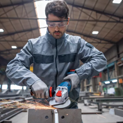 Homem a usar rebarbadora elétrica para cortar metal numa oficina industrial