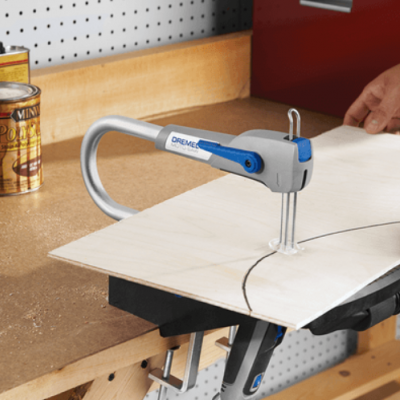 Serra tico-tico azul e cinza a cortar madeira clara numa bancada com latas de verniz