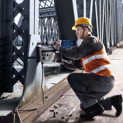 Trabalhador com capacete e colete refletor a operar equipamento numa ponte metálica