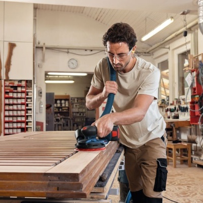 homem a lixar madeira com lixadora elétrica na oficina