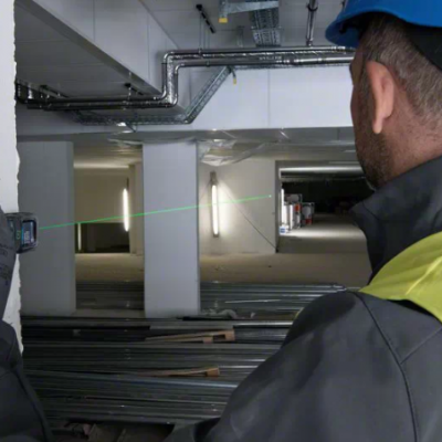 Homem com capacete azul e colete amarelo usando medidor a laser em construção interior
