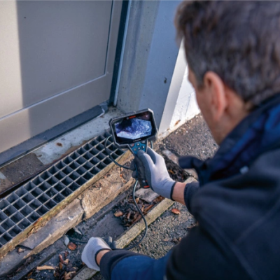 Homem a usar câmara de inspeção junto a ralo metálico perto de porta cinzenta