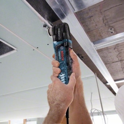 Pessoa a usar ferramenta elétrica BOSCH azul e preta em estrutura metálica no teto