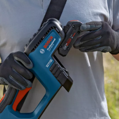 pistola de pregos Bosch azul e preto, com detalhes laranja, segurada por pessoa com luvas pretas