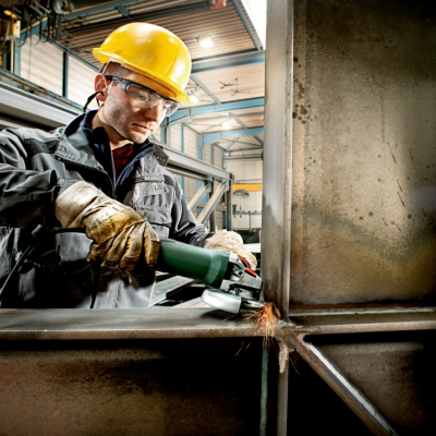 Trabalhador com capacete a usar rebarbadora numa estrutura metálica