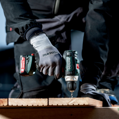 Parafusadeira elétrica preta e vermelha a ser usada em madeira, com luvas brancas.