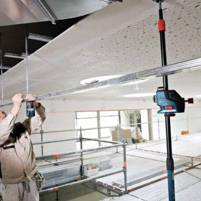 Trabalhador a instalar teto suspenso perfurado com ferramenta e tripé