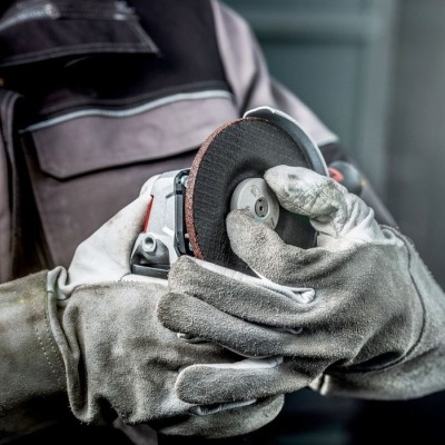 Pessoa com equipamento de proteção a segurar uma rebarbadora com disco abrasivo.