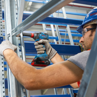Homem com capacete e luvas a usar ferramenta eléctrica BOSCH numa estrutura metálica.