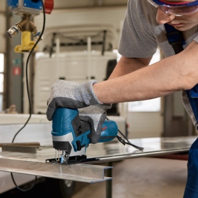 Pessoa a cortar metal com serra tico-tico em ambiente industrial