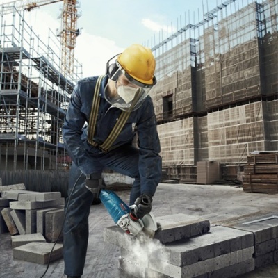 Trabalhador a cortar blocos de cimento com ferramenta elétrica em canteiro de obras