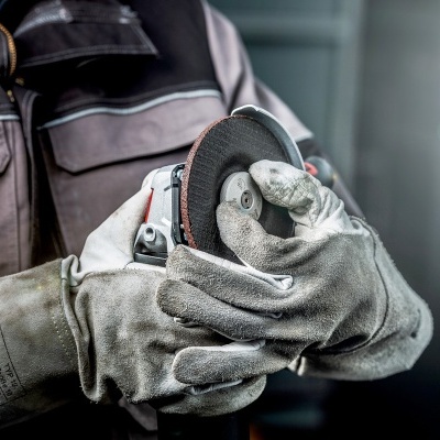 Pessoa com luvas segurando esmerilhadora angular em ambiente industrial